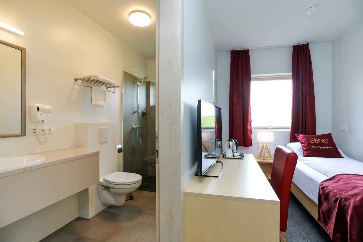 Ein Hotelzimmer mit Bad, einem Bett, einem Schreibtisch und einem Fernseher.