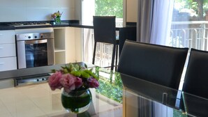 Une cuisine moderne dotée d’appareils électroménagers en acier inoxydable, un coin repas avec des chaises noires et une vue sur la verdure environnante.