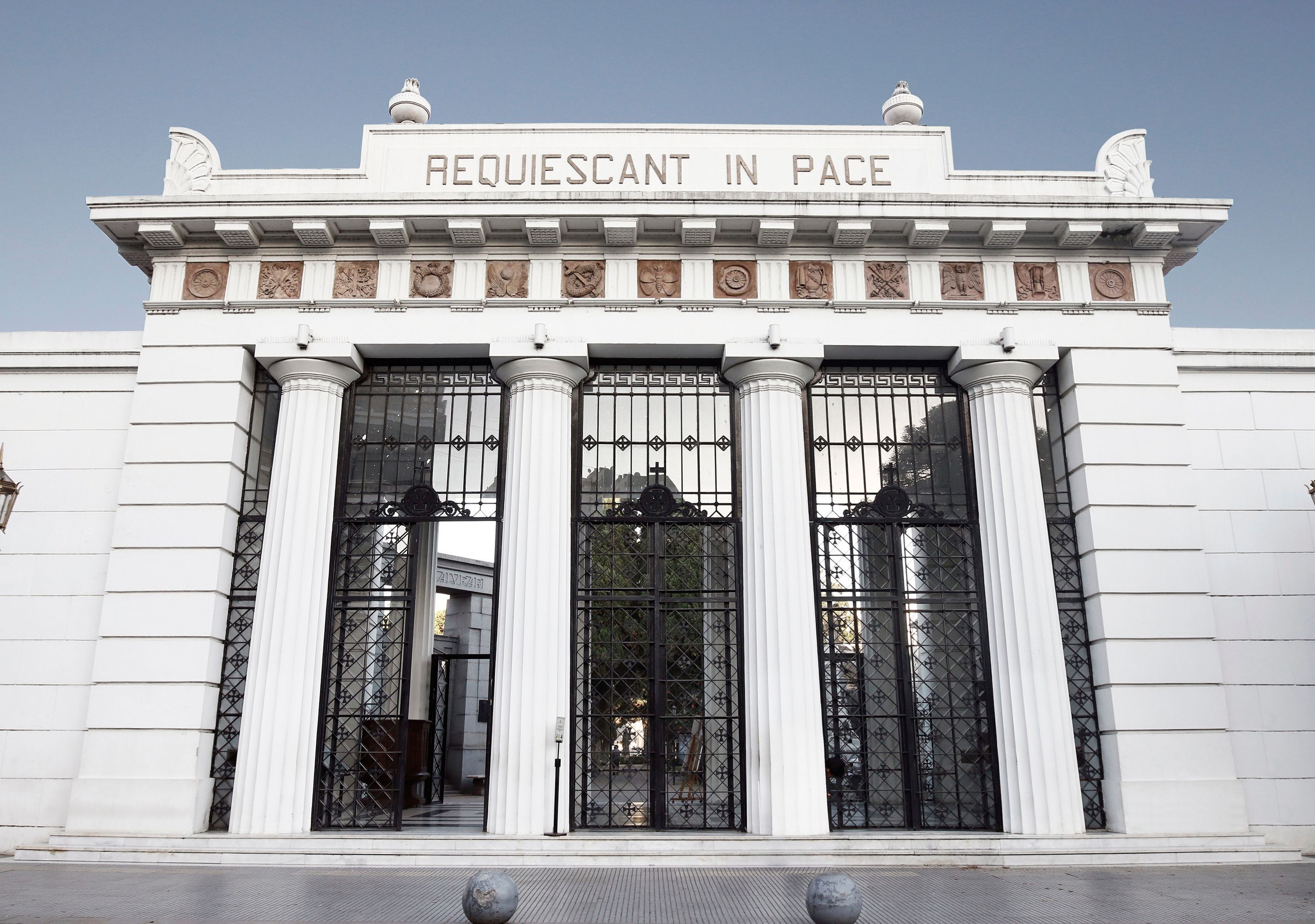 Fachada de edificio con la inscripción 'REQUIESCANT IN PACE' sobre un conjunto de columnas y un gran portón de entrada.