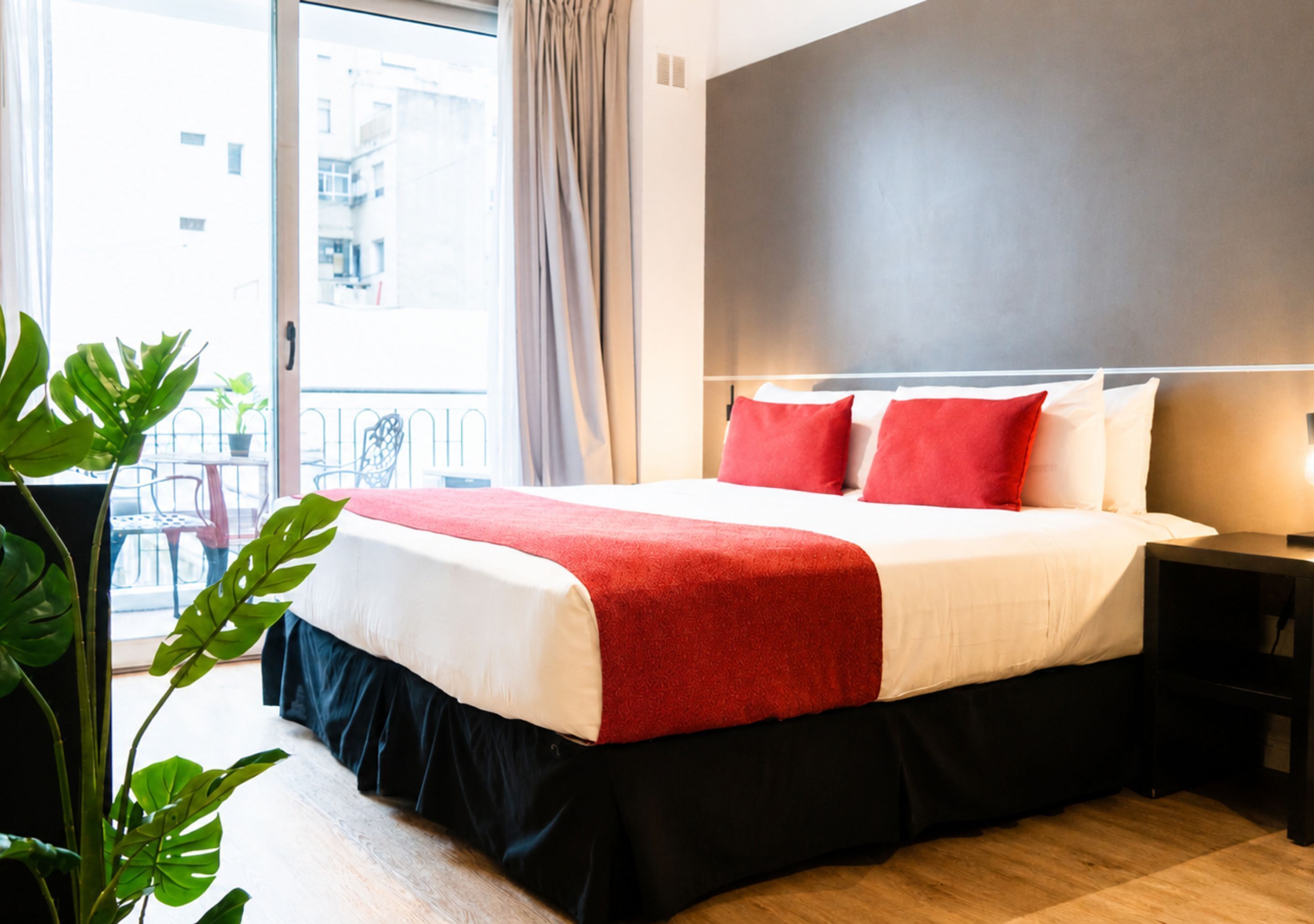 Quarto de hotel com uma cama grande, mesa de cabeceira, cortinas e vista para prédios.
