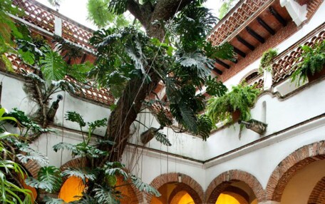 Un patio interior con zona de estar central, rodeado de arcos y abundante vegetación.
