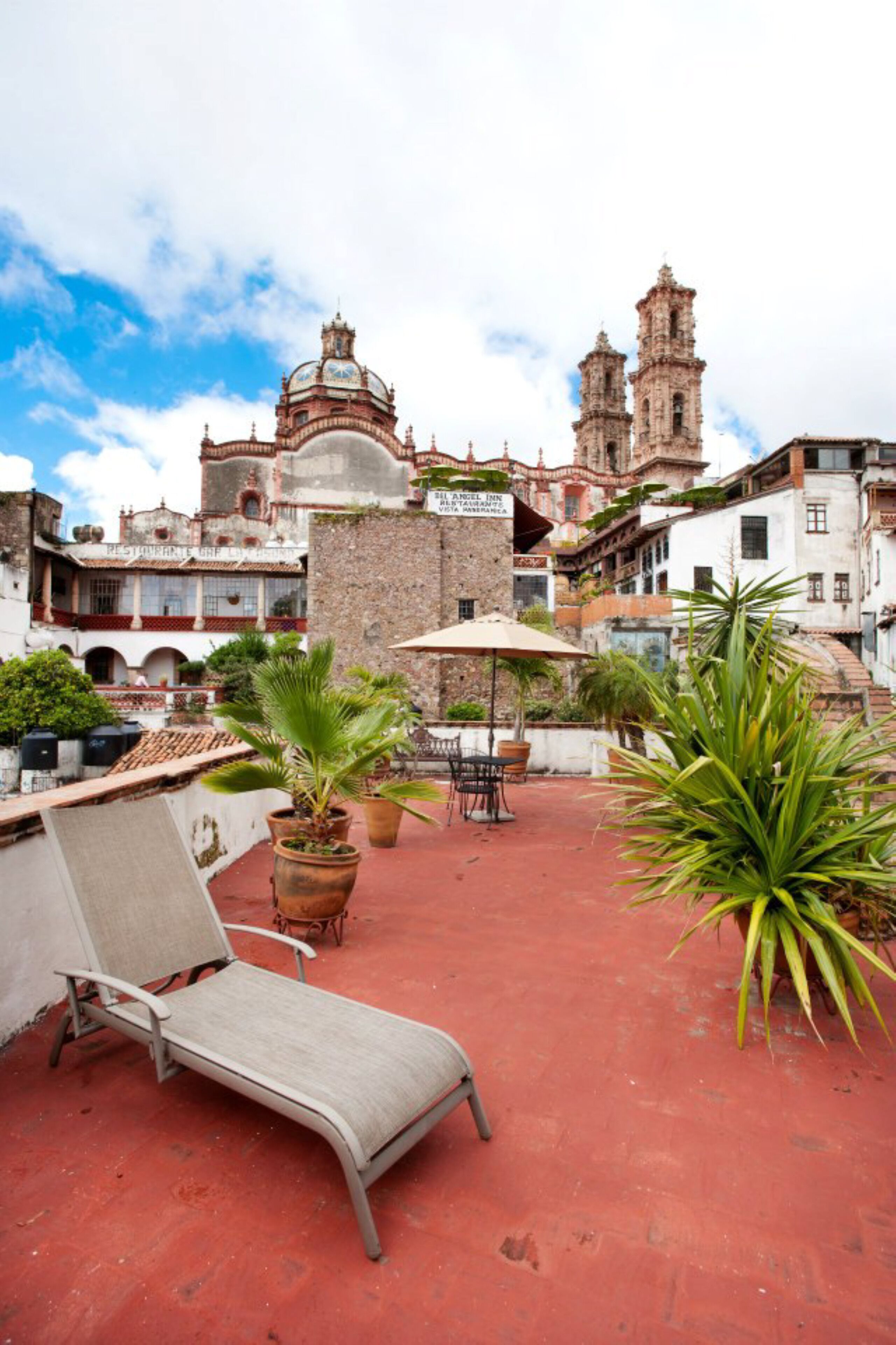 A rooftop terrace with a lounge chair, potted plants, and a view of historic buildings.