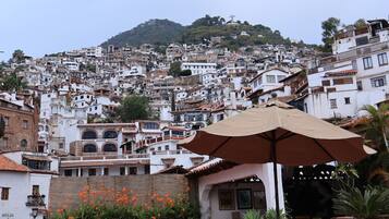Un patio con mobiliario exterior y plantas en macetas, con vistas a una ladera densamente poblada de arquitectura tradicional.