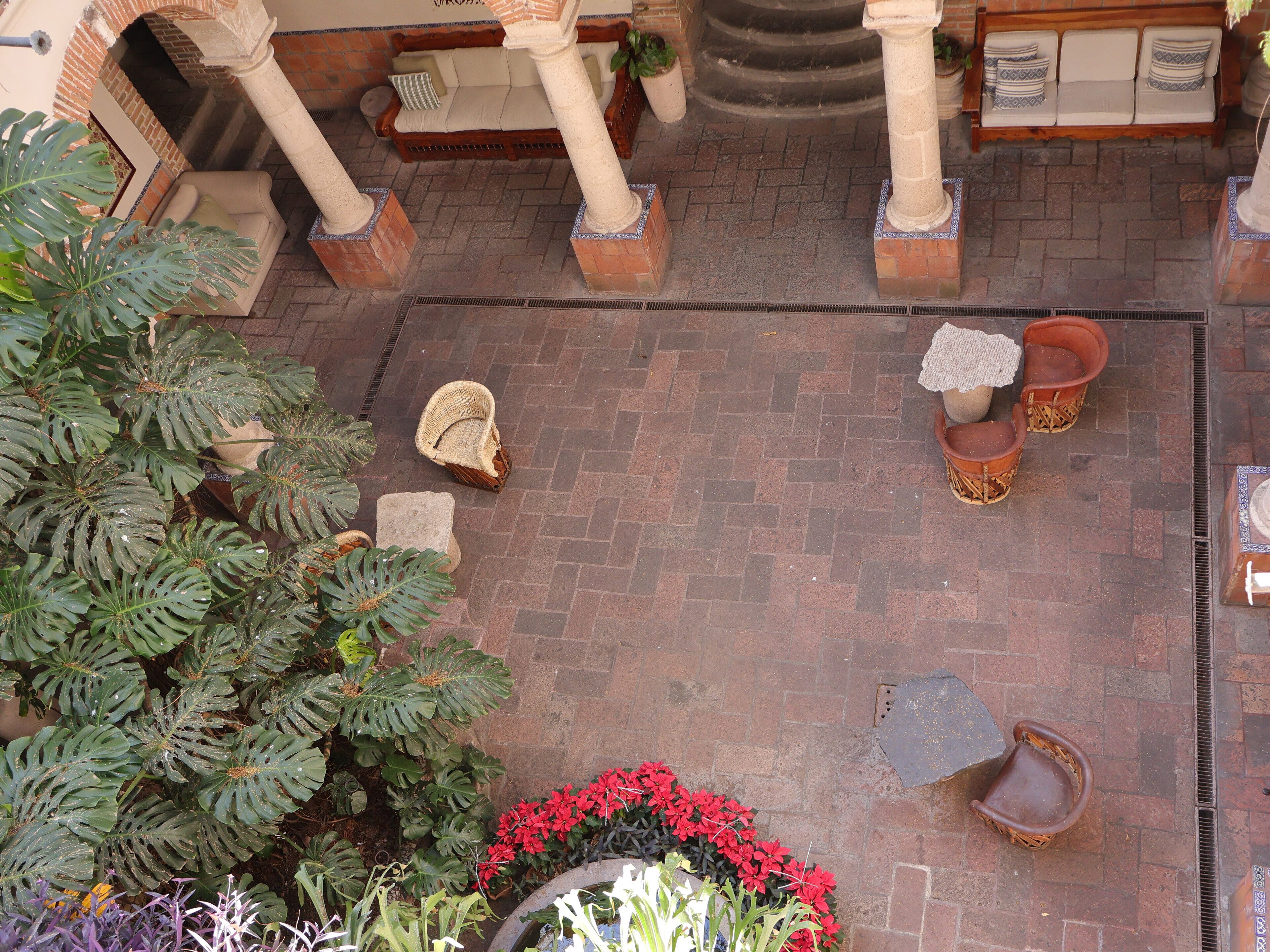 A courtyard with a brick floor, a wooden bench, potted plants, and a stone column.