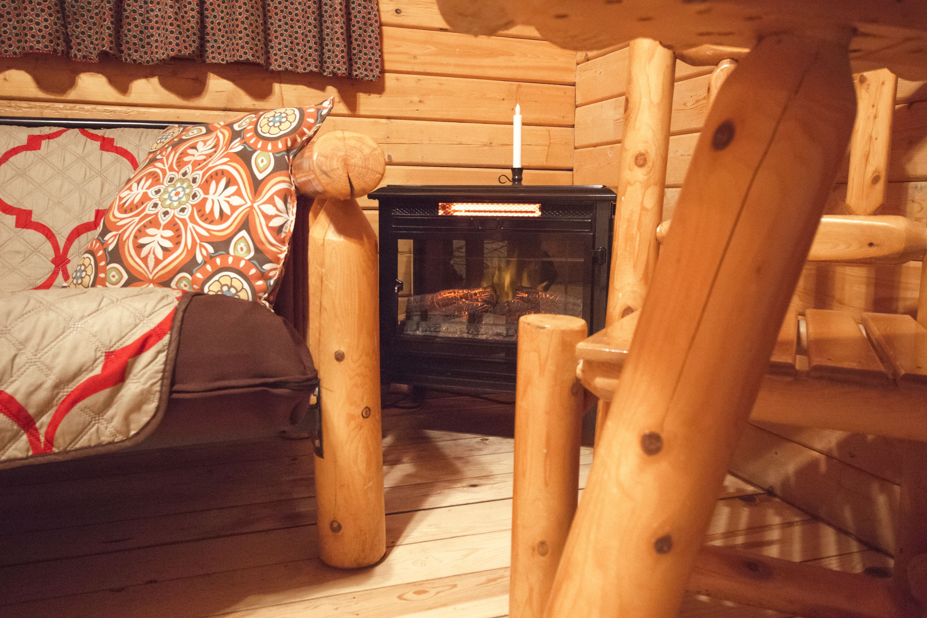 Interior acolhedor de uma cabana com uma cama de madeira, um cobertor acolchoado e uma lareira a lenha.