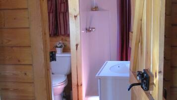 A wooden cabin bathroom with a toilet, sink, and shower.