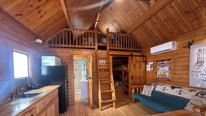 Interior de una cabaña de madera con cocina, comedor y habitación en altillo.