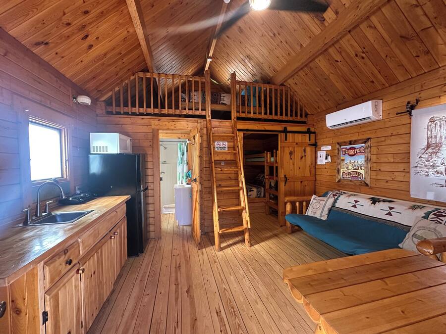 Interior de una cabaña de madera con cocina, comedor y habitación en altillo.