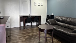Una sala de estar con un sofá de cuero marrón, una mesa de centro de madera, un escritorio con dos sillas y un microondas sobre una mesita auxiliar.