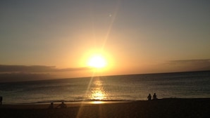 Atardecer sobre una playa con gente y un perro.