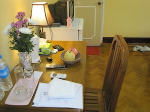 Una mesa de comedor con un florero, un control remoto, una cesta con una pera y una botella de loción.