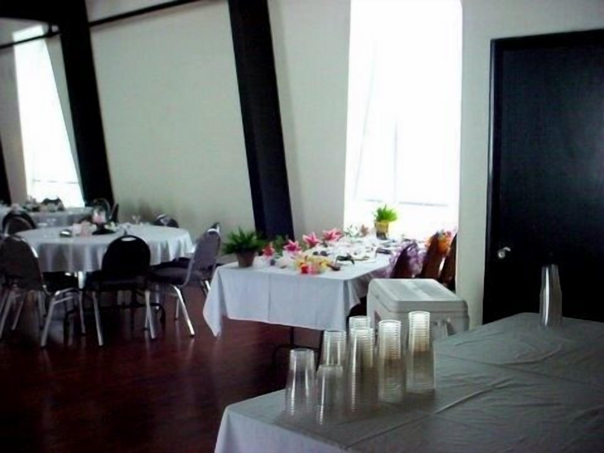 A dining area with round tables covered in white tablecloths, chairs, and a buffet table with stacked plates.