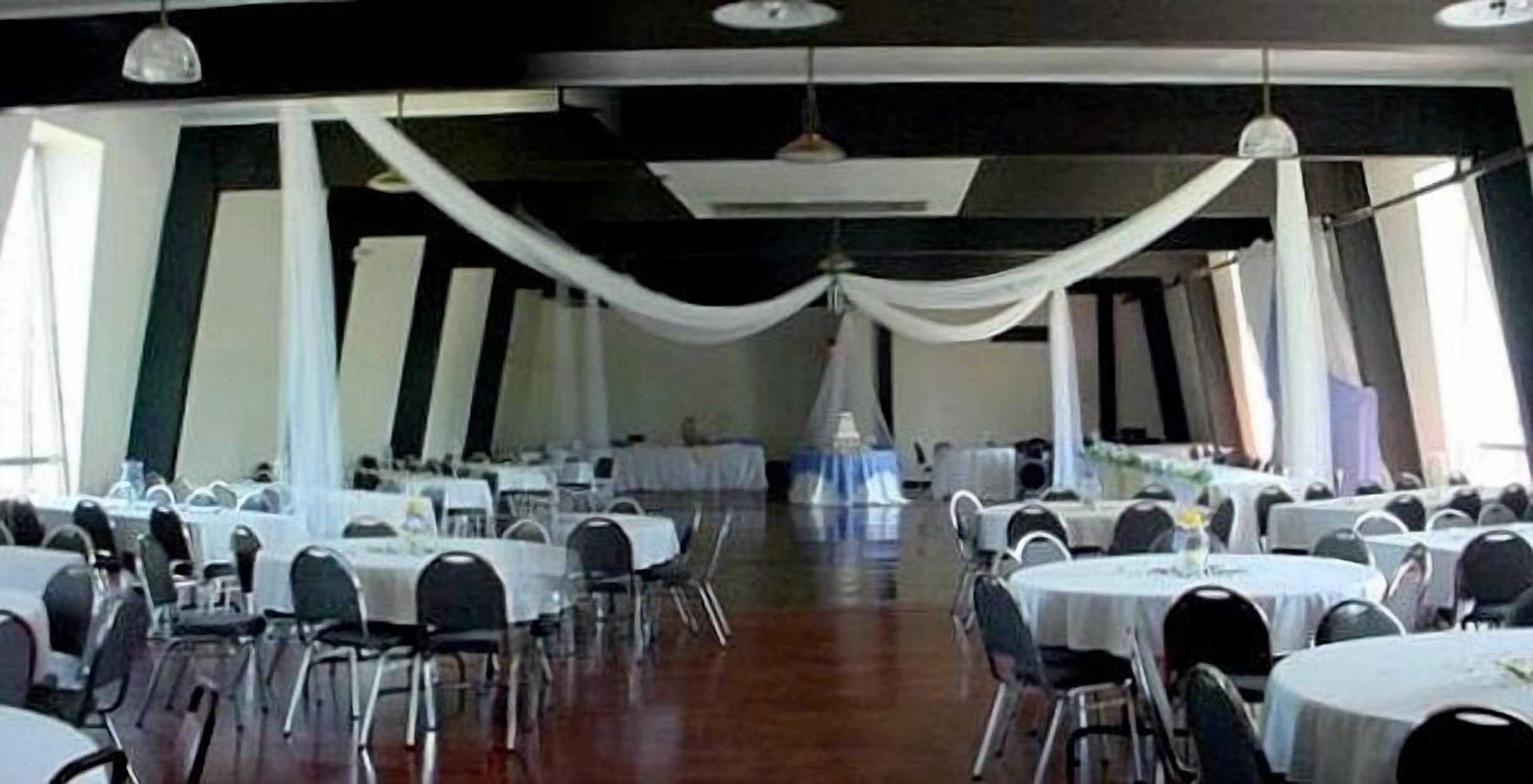 A conference room with round tables and chairs, white drapes hanging from the ceiling, and large windows on one side.