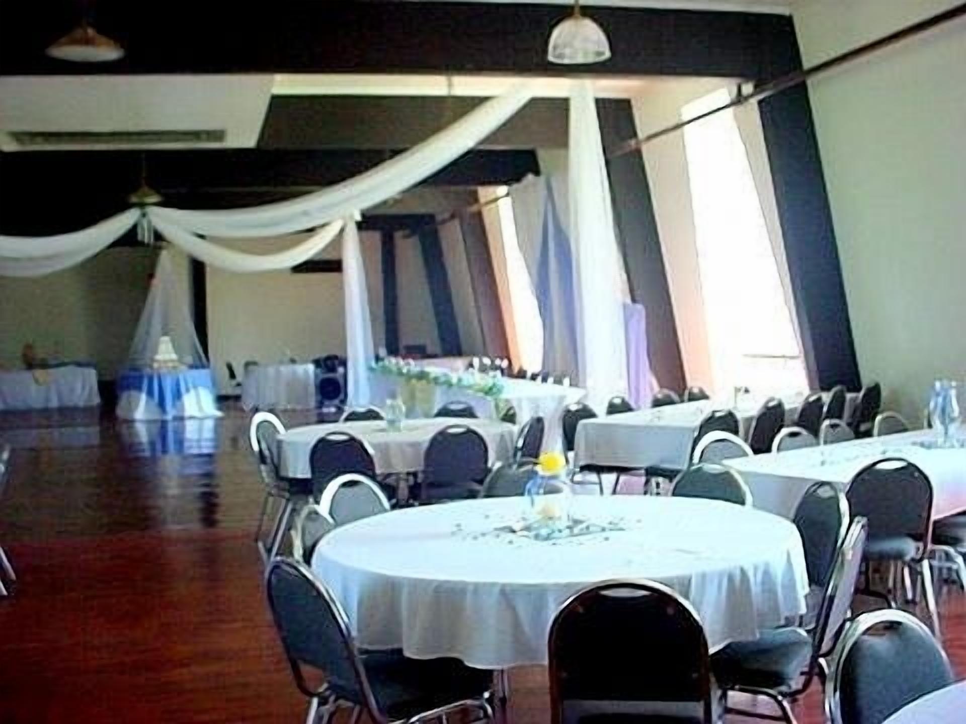 A banquet hall with round tables covered in white tablecloths, arranged in rows with chairs.