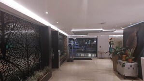 A hotel corridor with a decorative black wall, a reception area, and a potted plant on a cart.
