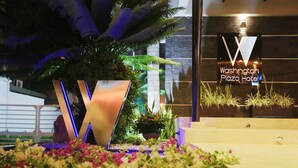 A hotel entrance with a large illuminated 'W' sign, a potted plant, and a flower bed.