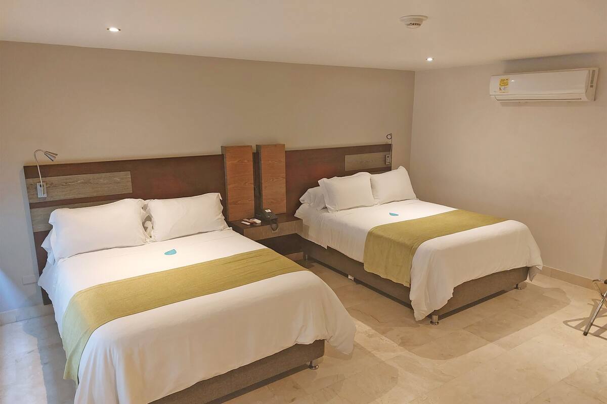 A hotel room with two beds, a nightstand, a lamp, and an air conditioning unit.