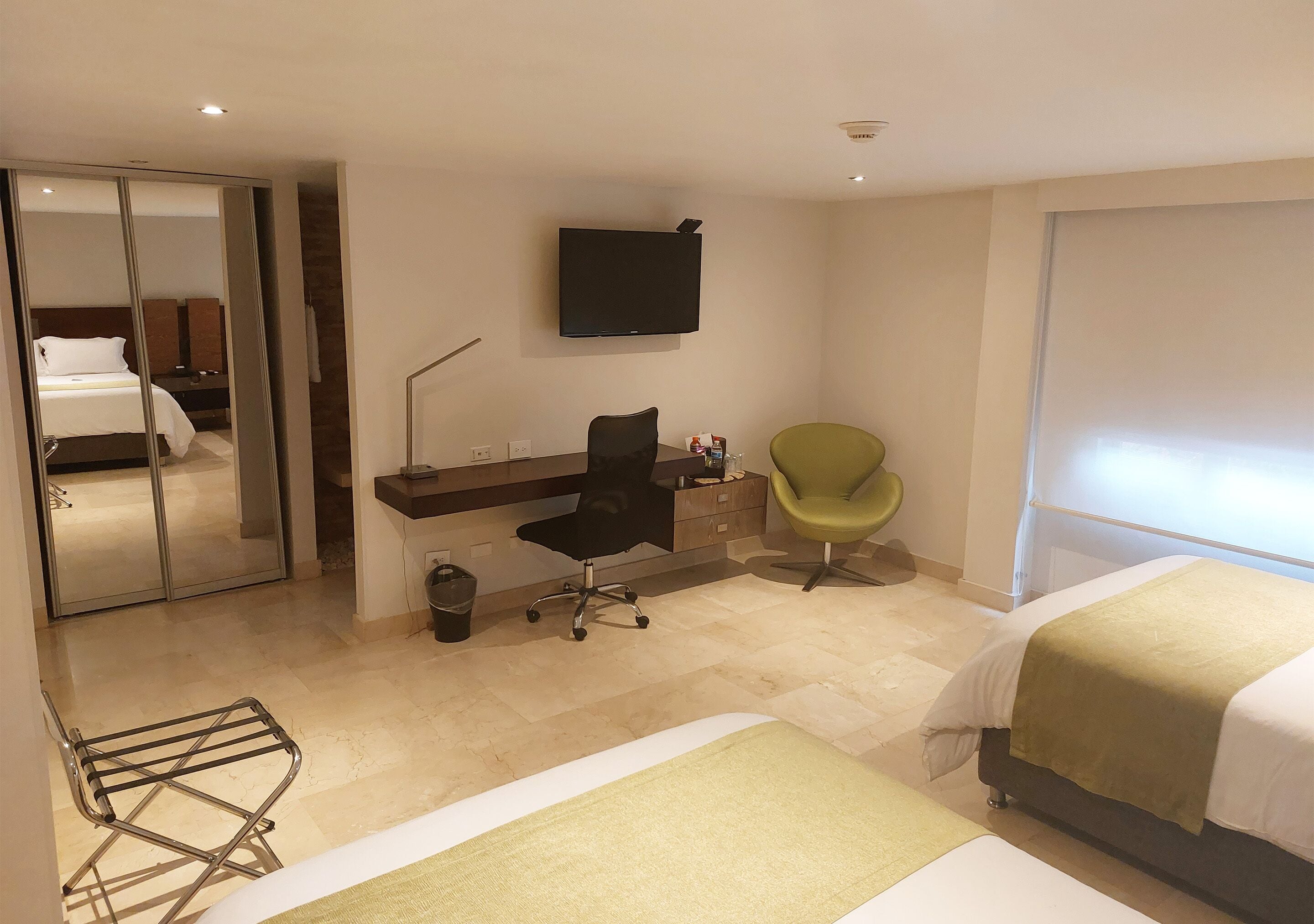 A hotel room with a bed, a desk with a chair, a television, and a mirror.