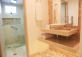 Un baño con ducha envuelta en vidrio, un lavamanos grande con encimera de mármol y un espejo con un revestimiento de madera.