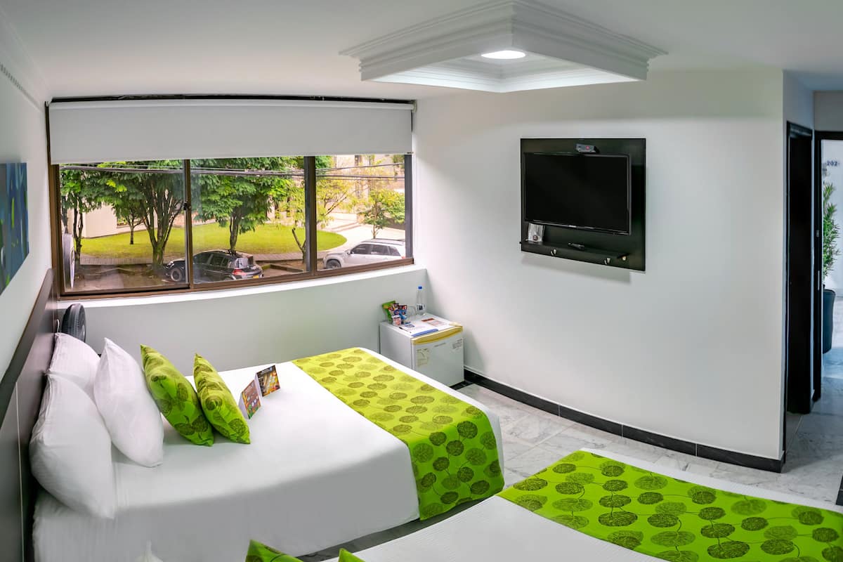 Une chambre d’hôtel avec deux lits, une télévision, un petit bureau et une fenêtre donnant sur l’extérieur.