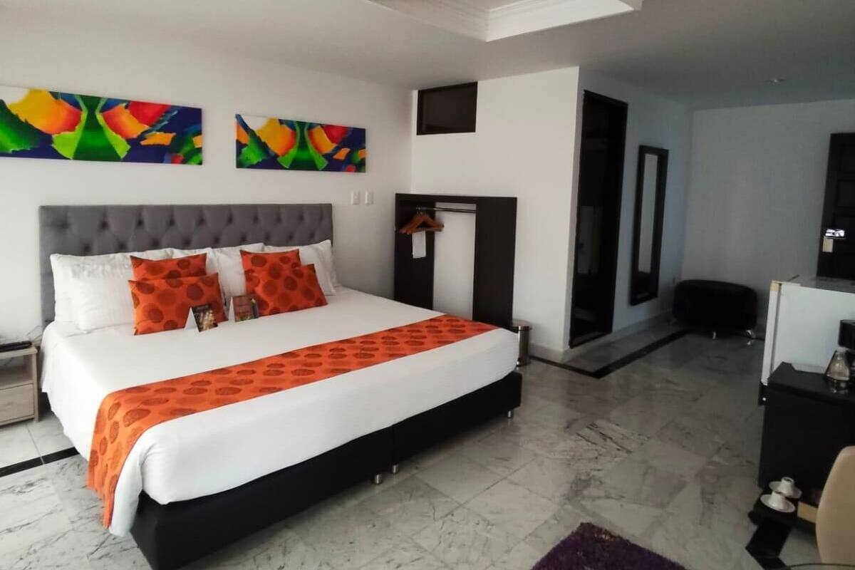 Une chambre d’hôtel moderne avec un grand lit, un bureau et une peinture abstraite aux couleurs vives accrochée au mur.