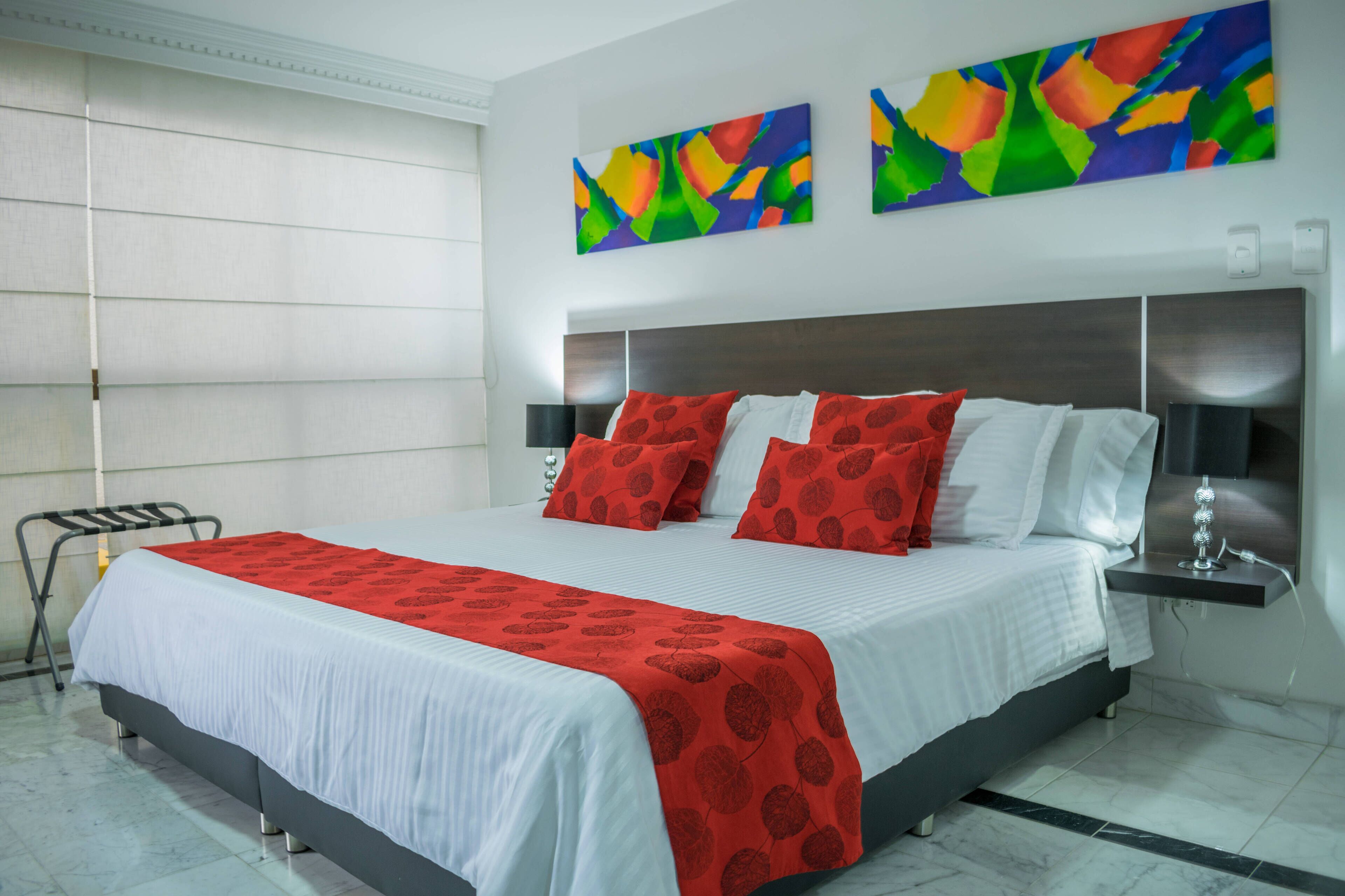 A modern hotel room with a large bed, a bedside table, a lamp, and abstract art on the wall.