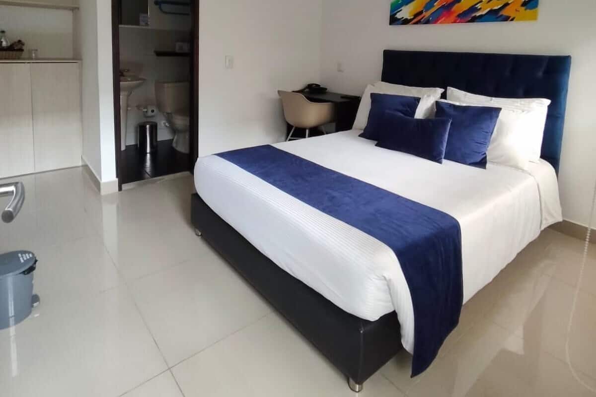 Une chambre d’hôtel moderne, équipée d’un lit, d’un bureau et ornée d’un tableau abstrait aux couleurs vives.
