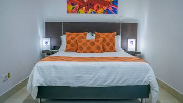 Habitación de hotel con una cama grande, dos mesitas de noche, un cuadro abstracto de colores sobre la cama y una pared blanca.