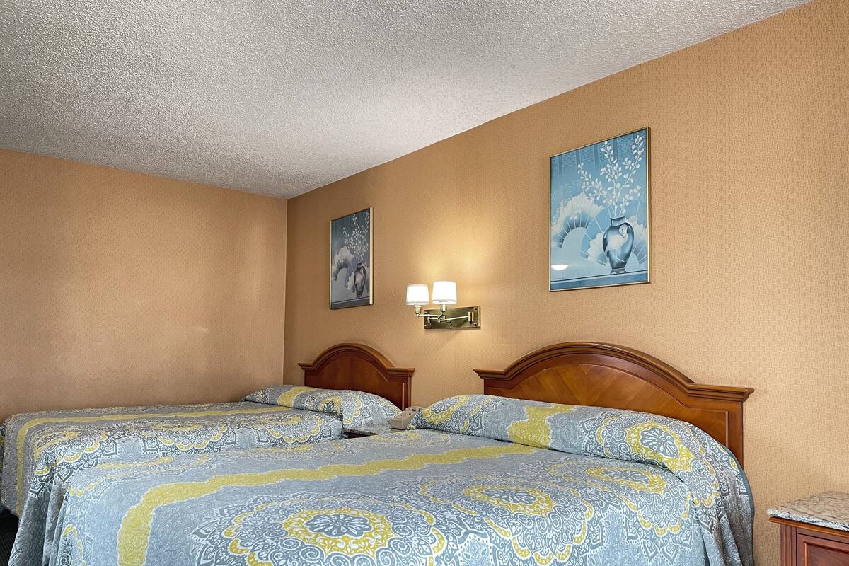 A hotel room with two beds, a wooden headboard, a wall-mounted lamp, and two framed artworks.