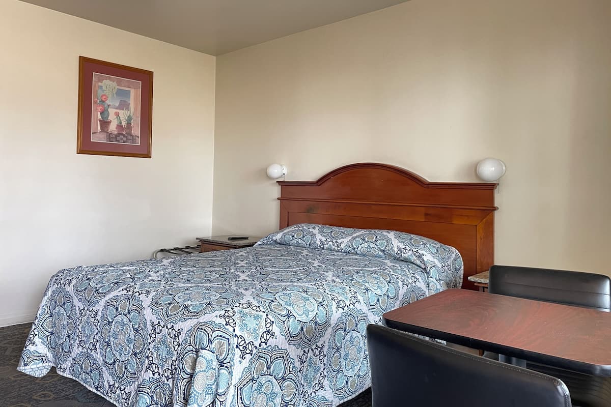 A hotel room with a bed, a wooden headboard, a table, and a chair.