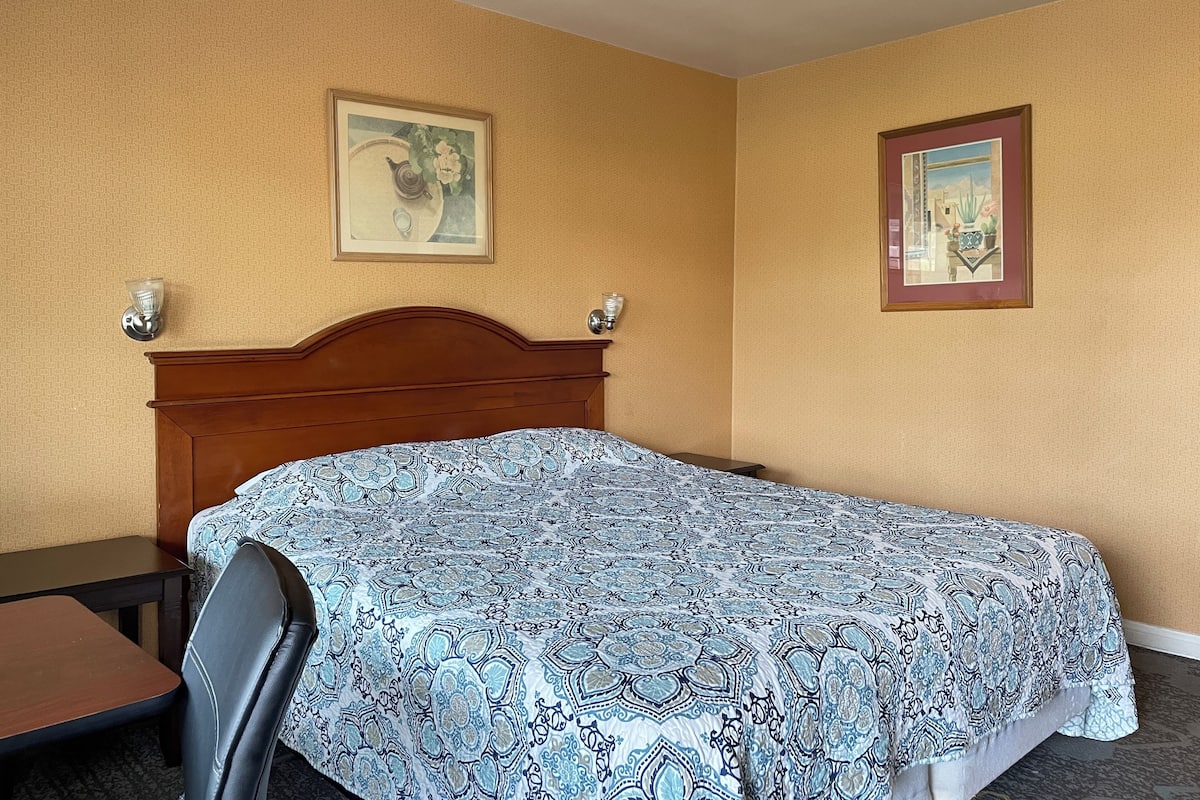 A hotel room with a wooden headboard, a patterned bedspread, a small table, and two wall-mounted lamps.