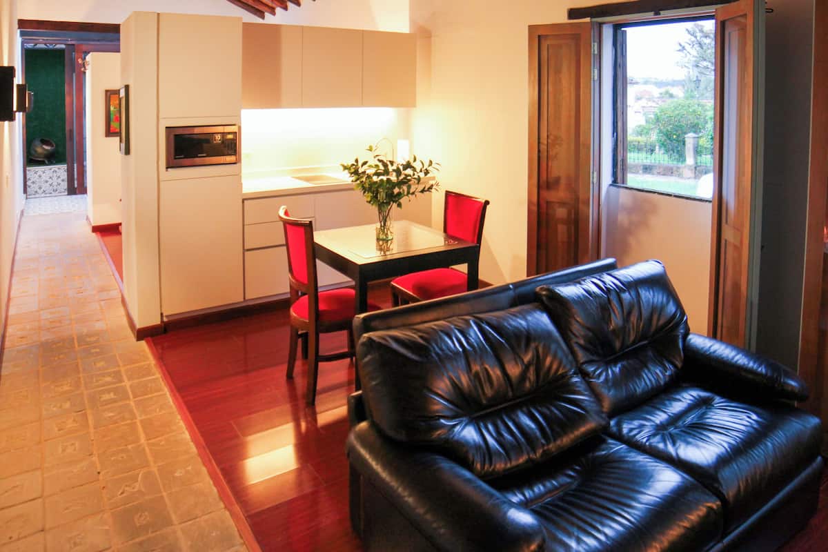 Una sala de estar moderna con un sofá de cuero negro, una mesa de comedor con sillas rojas y una zona de cocina con armarios blancos y un microondas.