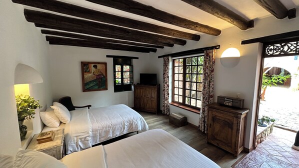 A bedroom with two beds, wooden beams, a painting, a TV, and a window with curtains.