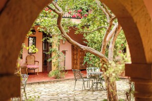 Une terrasse extérieure avec un sol en pierre, une porte en bois et une table entourée de chaises.