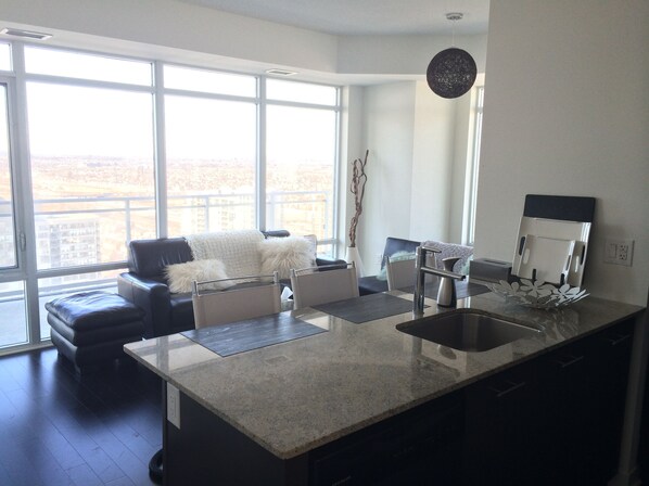 A modern kitchen with a large island, a dining area with a sofa, and a view of a cityscape through large windows.