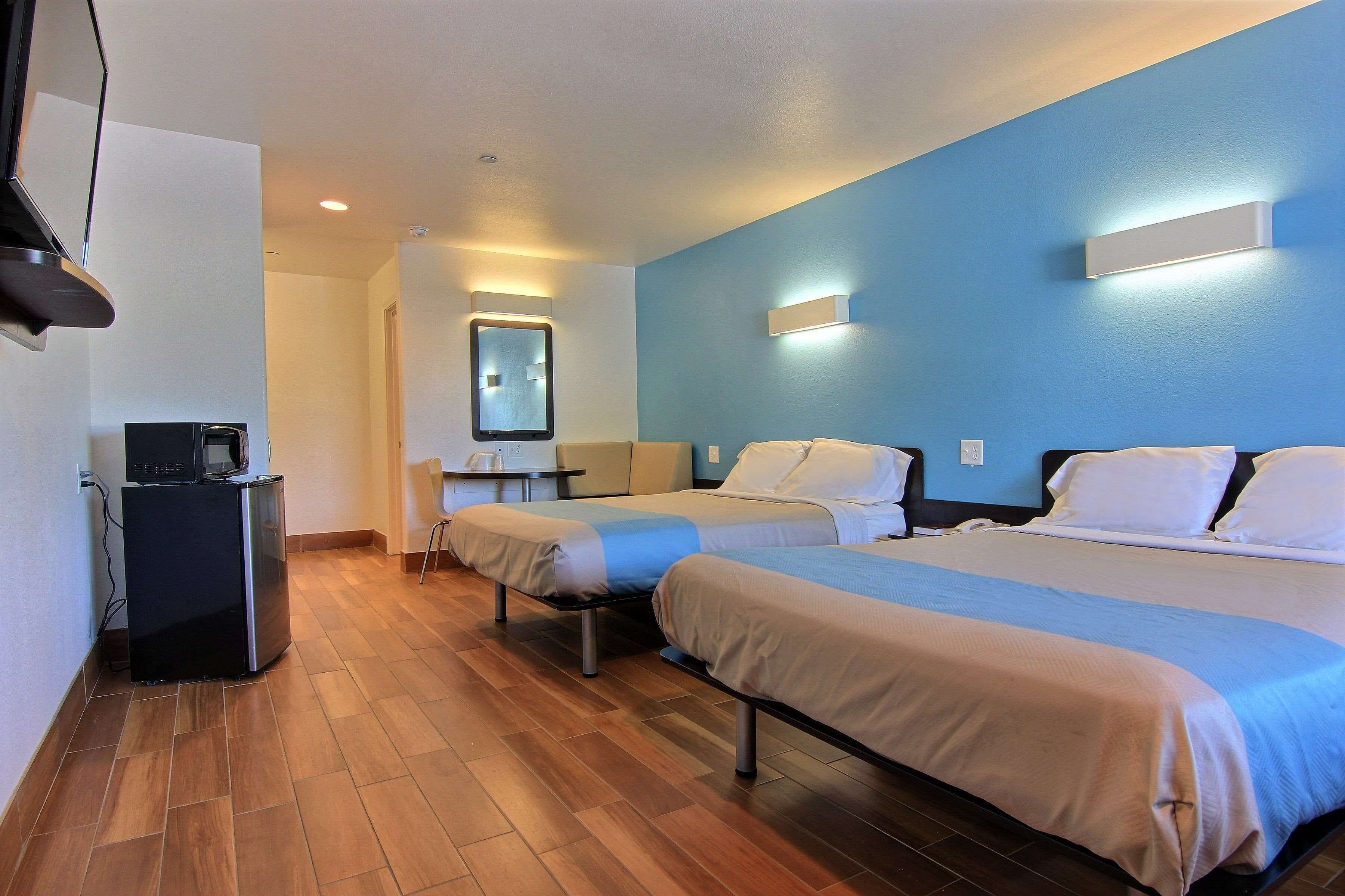 A hotel room with two beds, a small desk with a coffee machine, and a mirror on the wall.