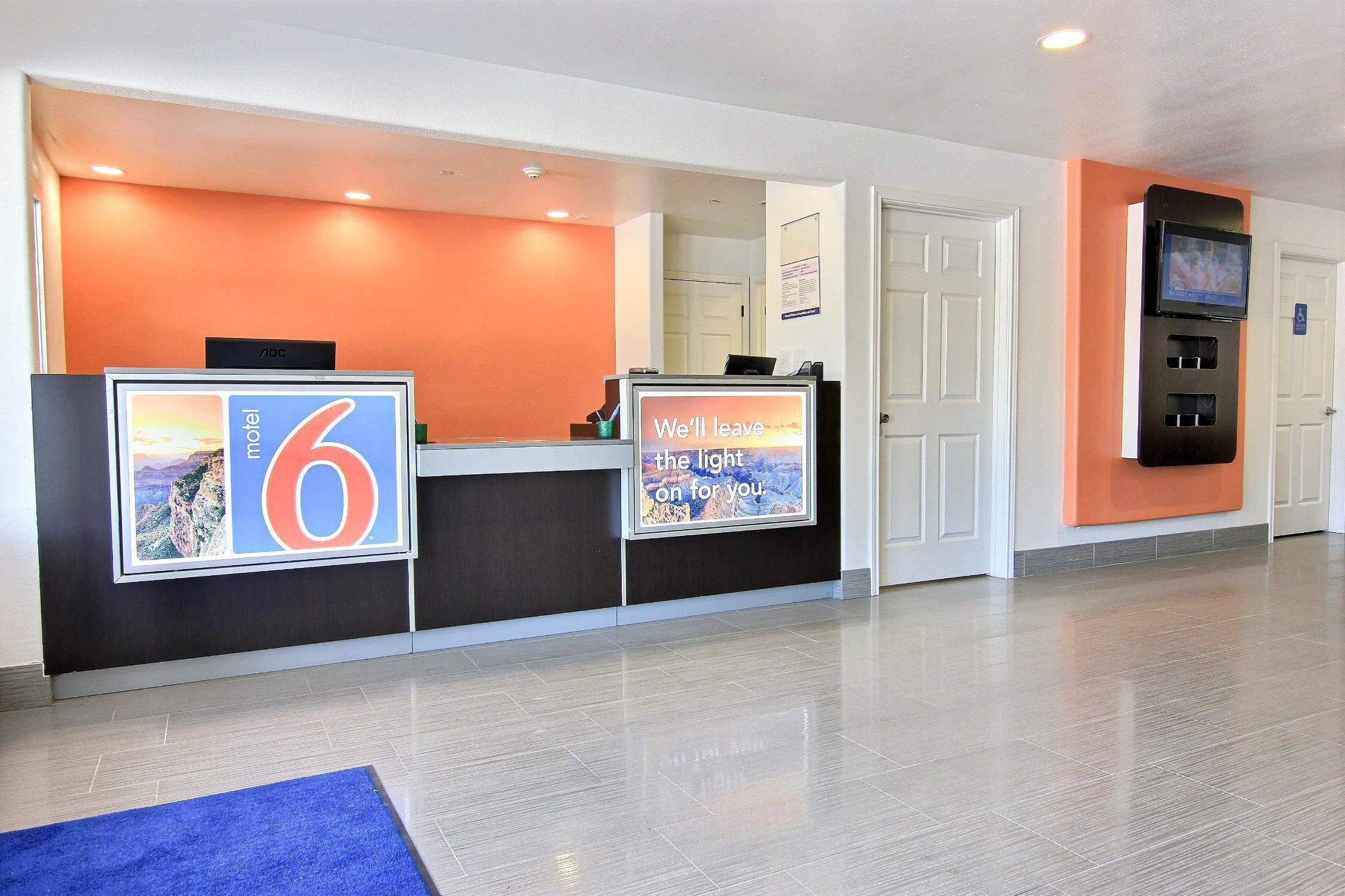 A hotel reception area with a large sign reading "6" and a message saying "We'll leave the light on for you."
