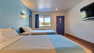 Ein Hotelzimmer mit zwei Betten, einem an der Wand befestigten Fernseher, einem Fenster mit Vorhängen und einer Tür.