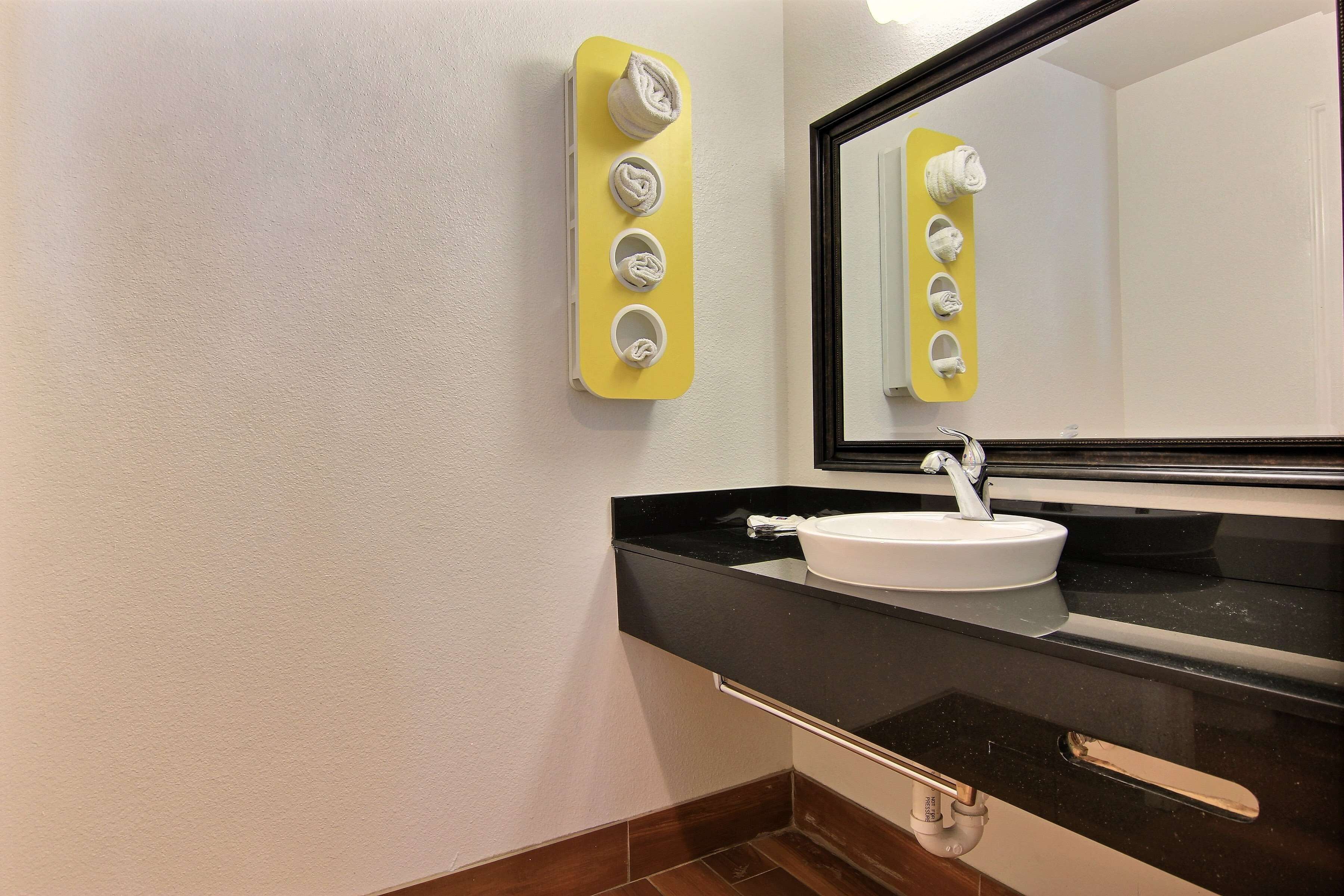 A bathroom with a white sink, black countertop, and a mirror with a yellow towel holder.