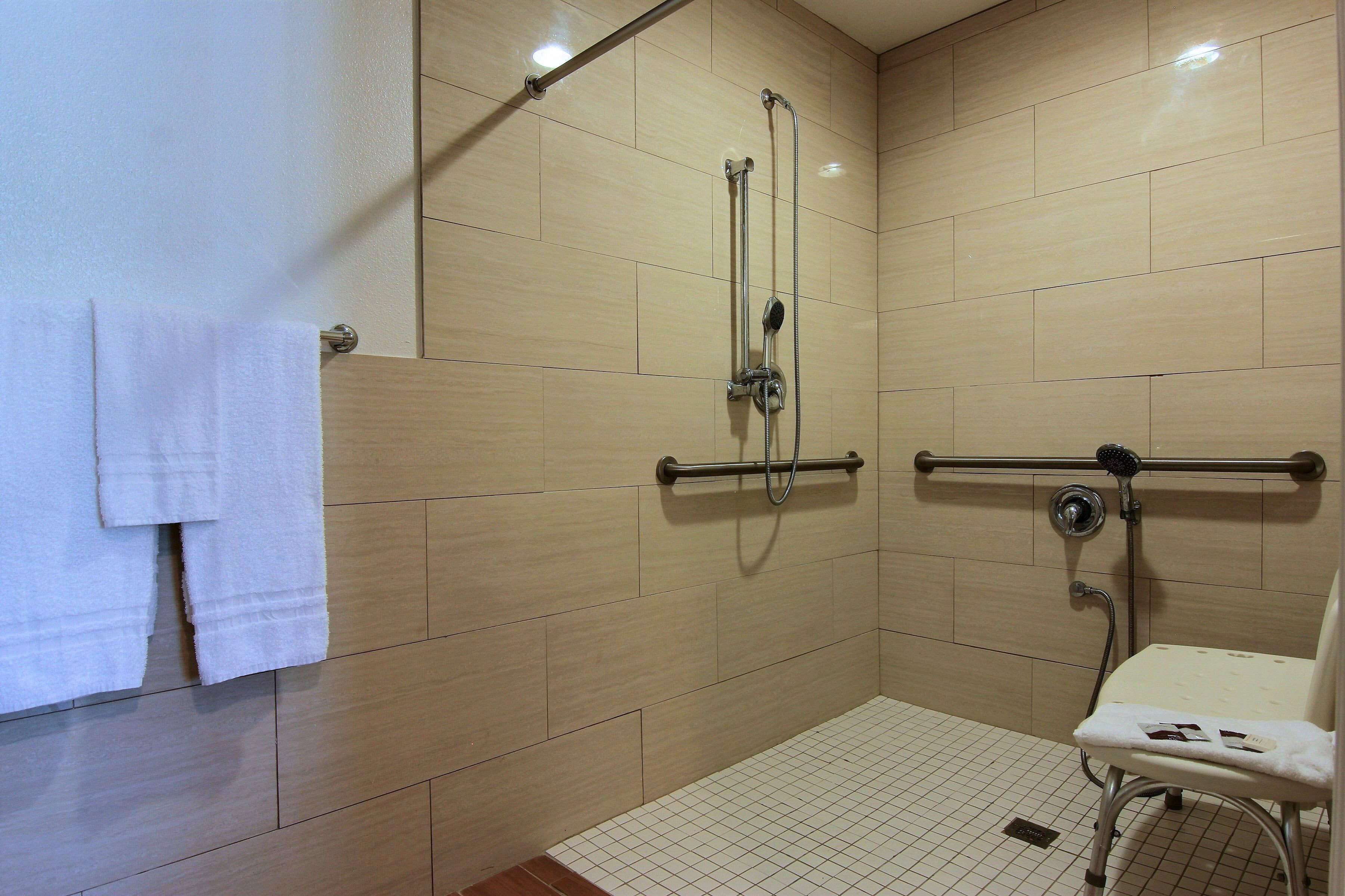 A shower area with a grab bar, a towel rack, and a chair.