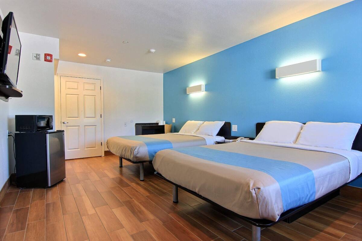 Quarto de hotel com duas camas, uma mesa, um pequeno frigorífico e uma televisão.