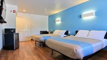 A hotel room with two beds, a desk, a small refrigerator, and a television.