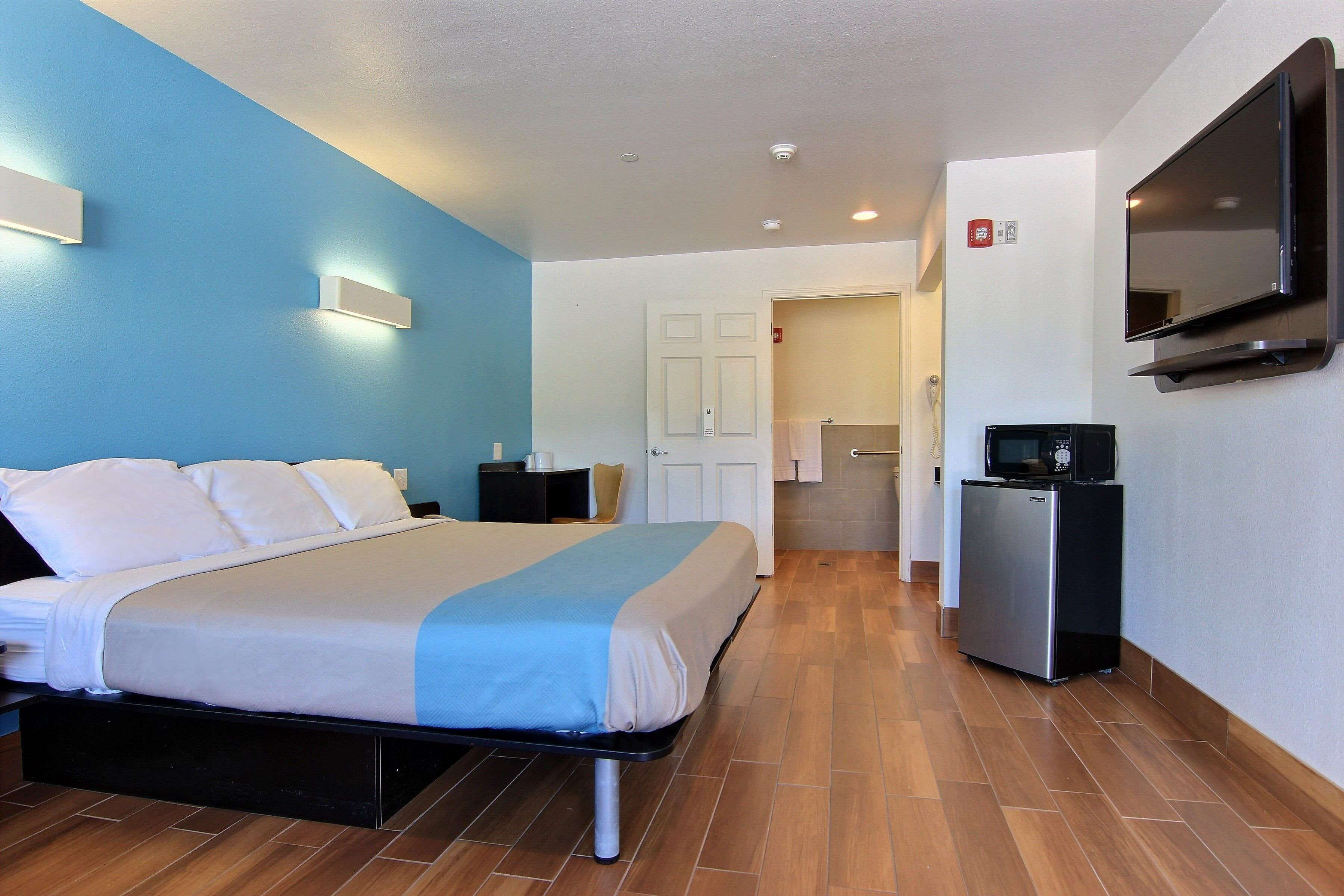 A hotel room with a bed, a TV, a small fridge, and a bathroom visible in the background.