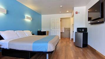 A hotel room with a bed, a TV, a small fridge, and a bathroom visible in the background.