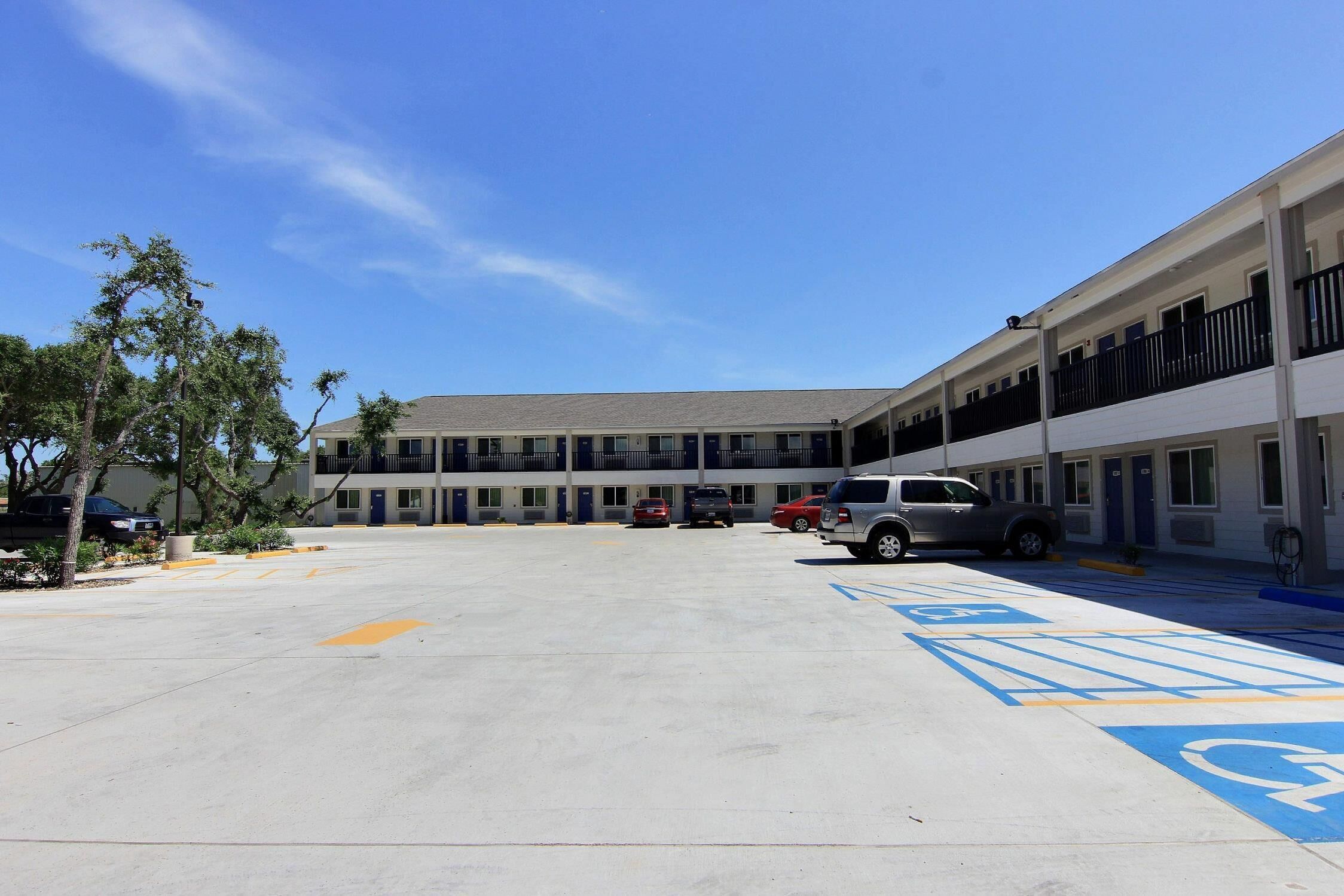A motel with a central parking area, multiple rooms on the ground floor, and a covered walkway.