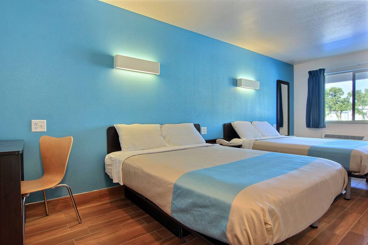 Quarto de hotel com duas camas, uma escrivaninha e uma cadeira.