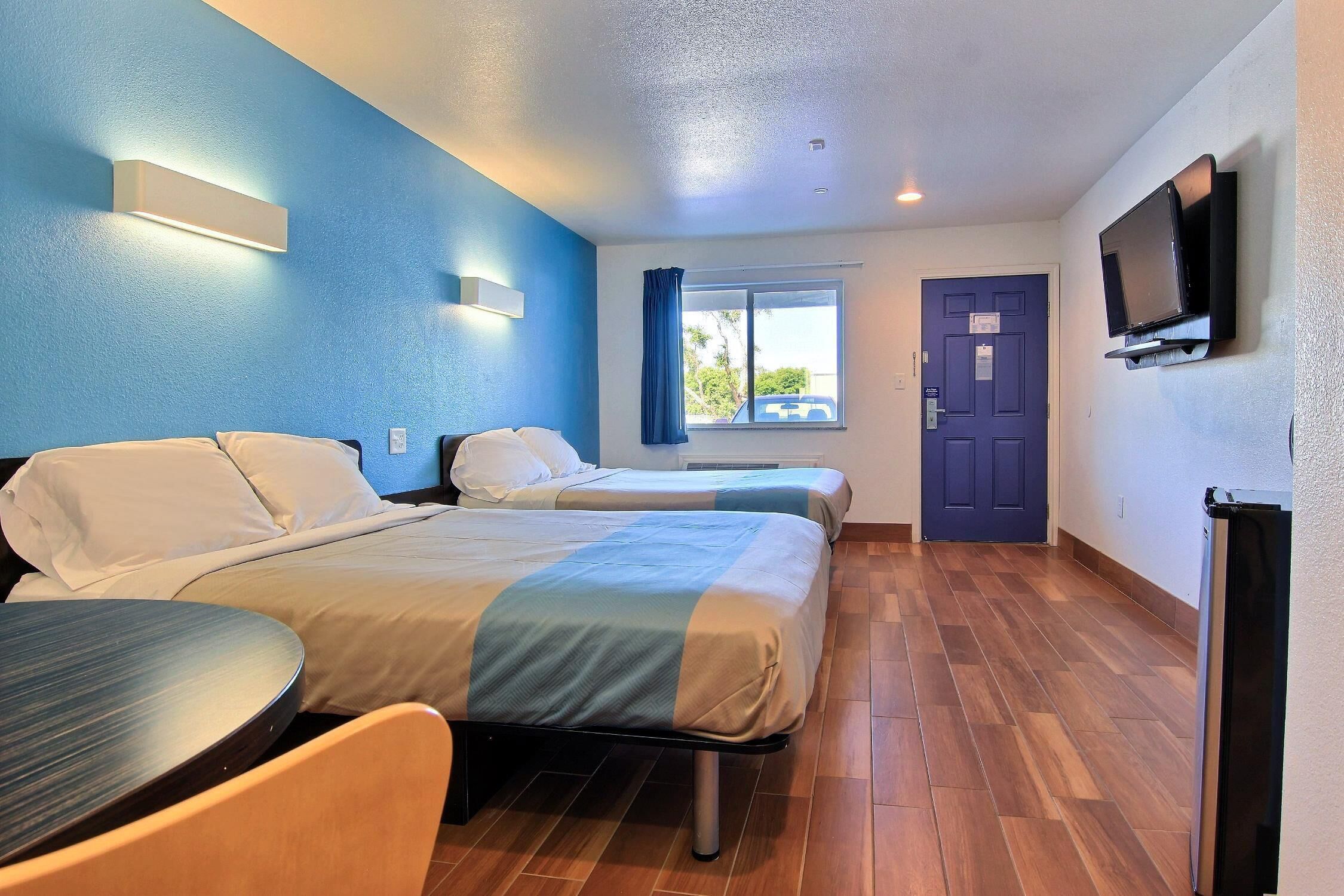 A hotel room with two beds, a TV mounted on the wall, and a window with curtains.