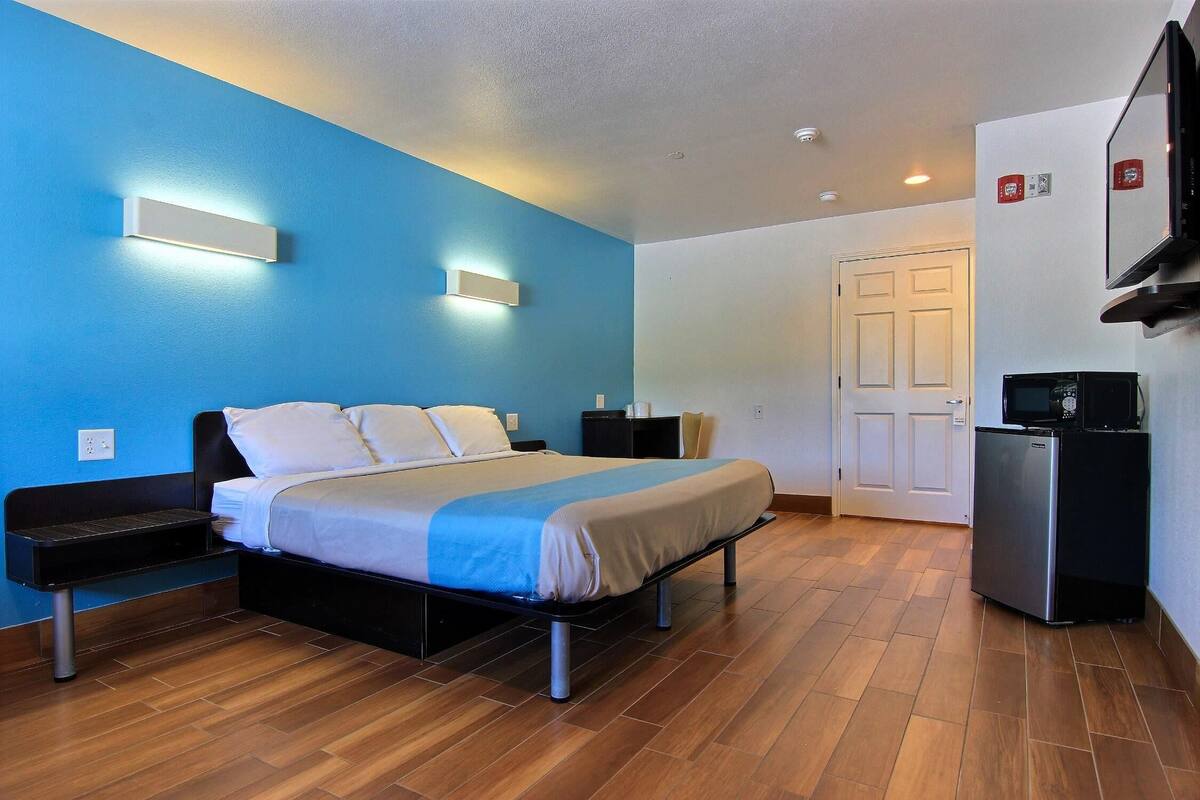 Quarto de hotel com cama, mesas de cabeceira, televisão, frigorífico e porta.
