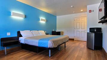 A hotel room with a bed, bedside tables, a TV, a refrigerator, and a door.