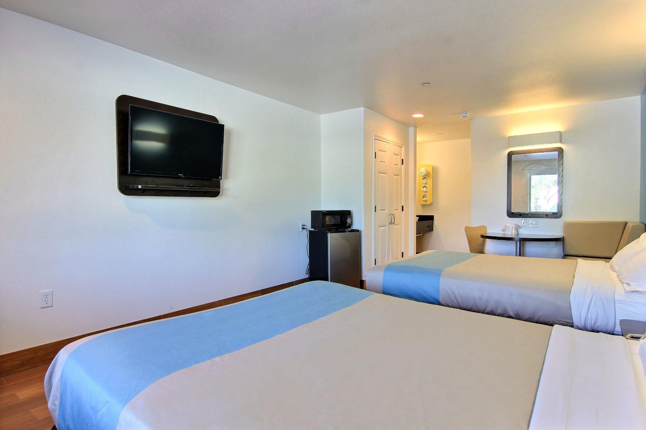 A hotel room with two beds, a television, a desk with a chair, and a microwave.